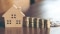 The picture shows a wooden model of a house with stacks of coins of decreasing height next to it.